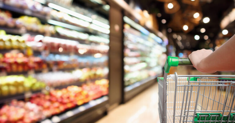 Woman's hand on a shopping cart handle with a blurred grocery store background